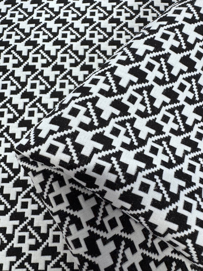 Designer - Brushstrokes - Black & White by Super Cheap Fabrics is a 148cm wide, 100% polyester fabric featuring a bold, geometric zigzag pattern with interconnected diamond and cross shapes. Two pieces are shown folded to display the repeating design.