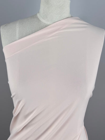 A close-up of a mannequin features Super Cheap Fabrics' ITY Knit - Baby Pink (150cm) draped diagonally across the torso, creating an elegant, asymmetrical one-shoulder look against a plain gray background.