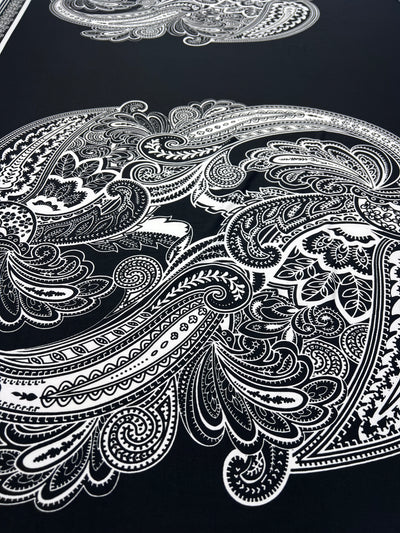 The Printed Lycra - Antoinette Paisley - 85cm Panel by Super Cheap Fabrics features intricate white paisley and floral patterns on dark medium-weight Polyester/Spandex, creating a bold, elegant look with swirling lines and delicate shapes.