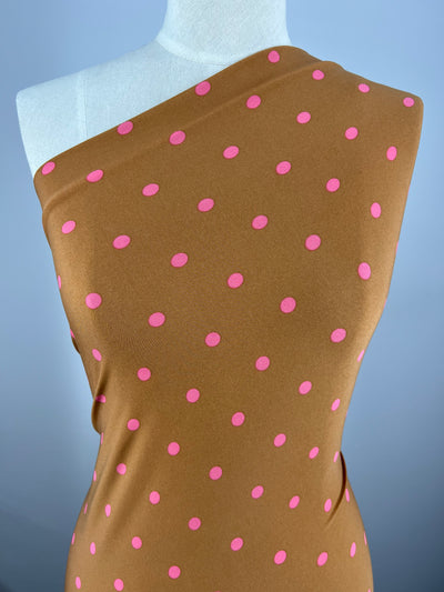 A dress form displays Super Cheap Fabrics' Printed Lycra - Pecan & Pink Polka - 150cm, a brown polyester spandex with a one-shoulder style and evenly spaced pink polka dots.