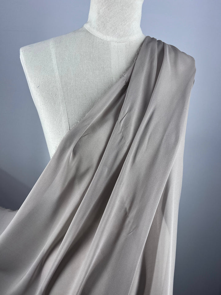 A mannequin is elegantly draped in Super Cheap Fabrics' Pure Silk Georgette - New Marble (135cm) on a gray background, showcasing the smooth texture and soft folds of this lightweight fabric—ideal for spring-summer outfits.