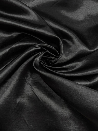 Shantung Satin - Black - 150cm from Super Cheap Fabrics features smooth black satin with a shiny finish, elegant texture, and soft highlights—perfect for adding sophistication to any design.