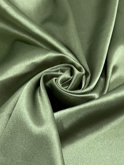 A close-up of Super Cheap Fabrics Satin Back Crepe - Epsom (150cm) in light olive green, gathered to highlight its soft texture and subtle sheen—ideal for elegant eveningwear and standout fashion pieces.
