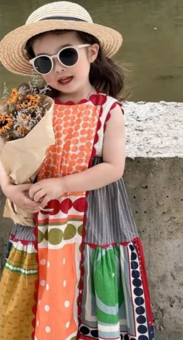 A young girl in a vibrant dress made from Designer Rayon - Stile - 145cm by Super Cheap Fabrics, with a straw hat and sunglasses, smiles while holding dried flowers in front of a stone wall.