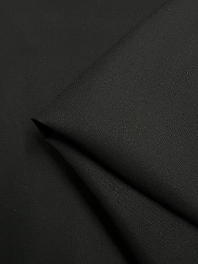 A neatly folded close-up of smooth, tightly woven Cotton Drill in black by Super Cheap Fabrics. This 150cm medium-weight fabric is crafted from 100% cotton, with a soft texture and subtle sheen.