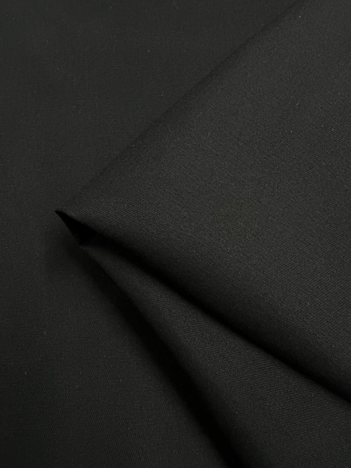A neatly folded close-up of smooth, tightly woven Cotton Drill in black by Super Cheap Fabrics. This 150cm medium-weight fabric is crafted from 100% cotton, with a soft texture and subtle sheen.