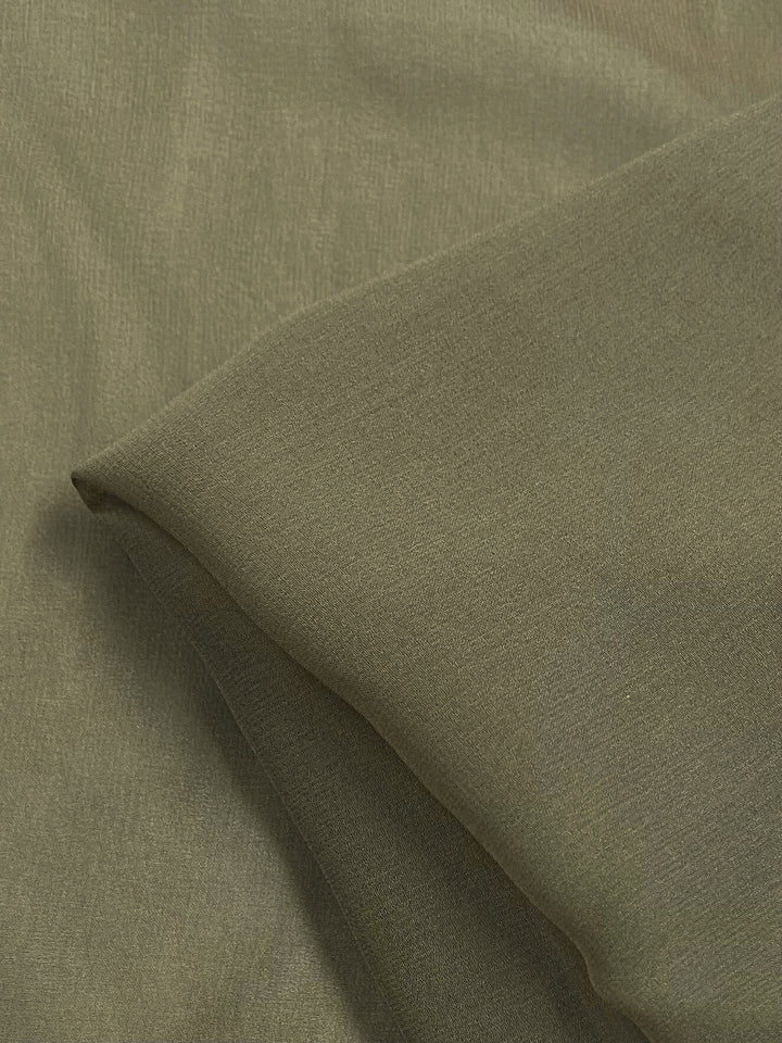 Close-up of olive green Pure Silk Georgette - Dune - 135cm by Super Cheap Fabrics with a smooth, lightly textured surface. This lightweight fabric is elegantly draped and subtly shiny, ideal for spring and summer attire.