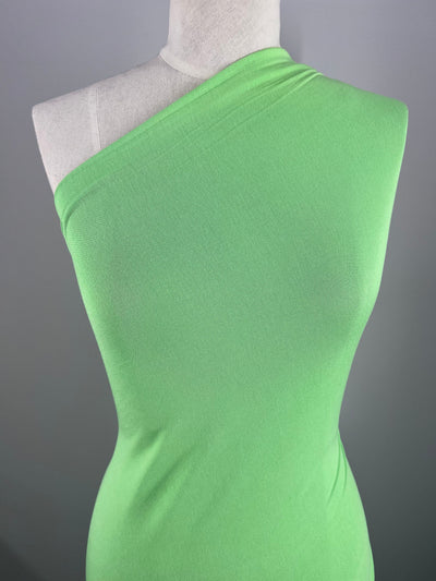 The Summer Cotton Knit - Paradise Green by Super Cheap Fabrics, elegantly displayed on a mannequin against a gray background, contours beautifully with its smooth cotton fabric and excellent stretch recovery.