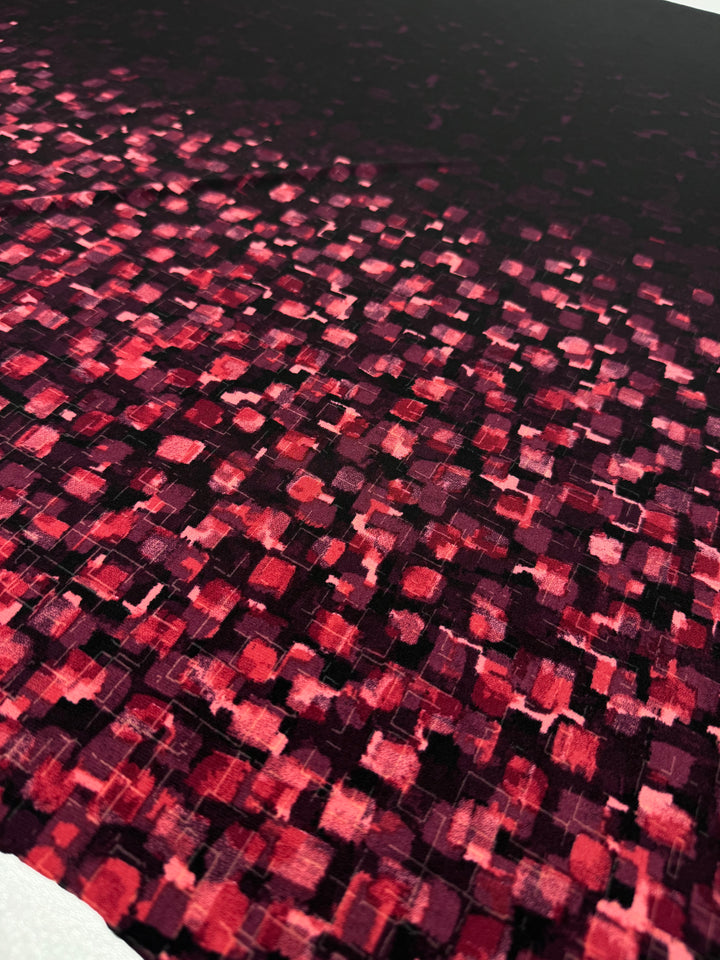 Close-up of the Designer Lycra Panel - 90cm Panel by Super Cheap Fabrics, featuring a dark surface with red and pink squares that fade into black toward the top, creating a pixelated, textured look across the fabric.