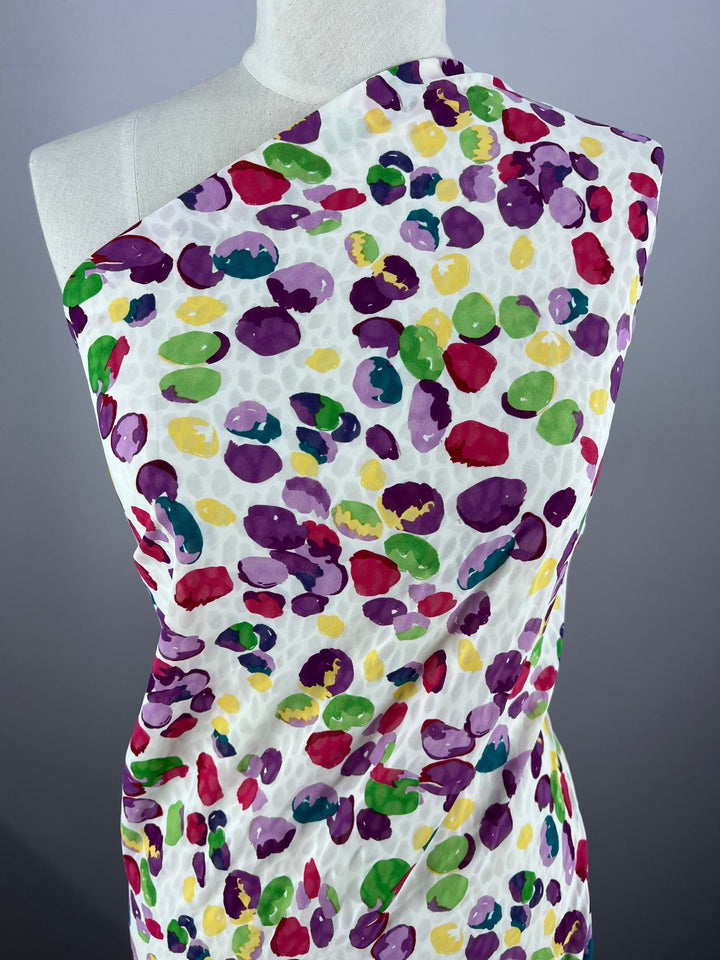 A Super Cheap Fabrics mannequin displays the elegant Salt Shrunk Print - Pebbly fabric in colorful purple, yellow, green, and red ovals on white. The 155cm fabric is draped over one shoulder for an asymmetric look.