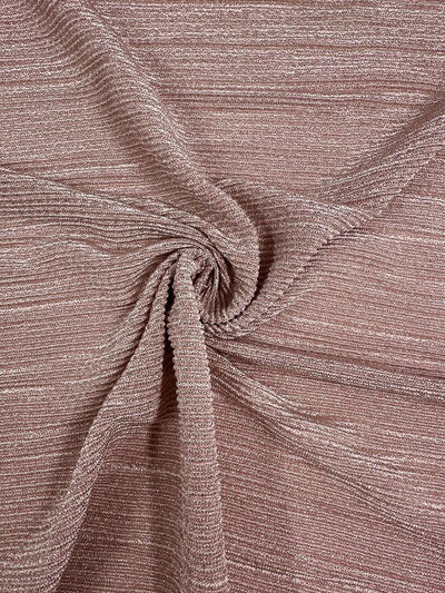 Close-up of a textured, blush-toned stretch fabric with a subtle pattern. The medium to heavy weight knit fabric from Super Cheap Fabrics is gathered and twisted at the center, creating a swirl effect. The Metallic Knit - Blush - 150cm appears soft and has a slightly lustrous sheen.