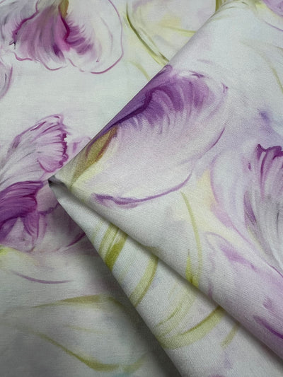 Peony Dreams designer cotton fabric with a whimsical peony print, featuring natural fibers in purples and whites. The fabric showcases peonies floating in the wind, ideal for creating breezy, elegant summer dresses that can be worn for casual outings or special occasions. Perfect for adding a touch of femininity and high-quality craftsmanship to your wardrobe, whether paired with sandals or heels.