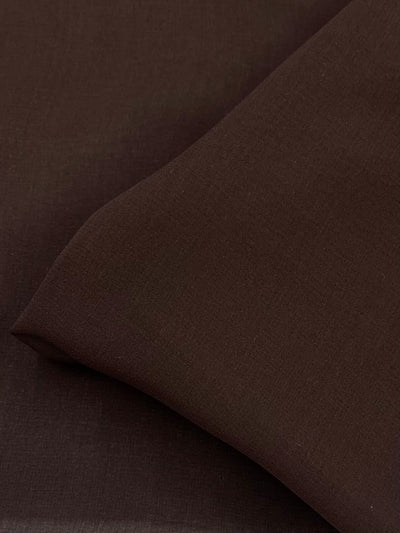 The close-up of "Pure Silk Georgette - Chocolate - 135cm" by Super Cheap Fabrics reveals a thick yet lightweight brown fabric with a silky texture, ideal for spring and summer outfits, with its neat creases casting subtle shadows and highlights.