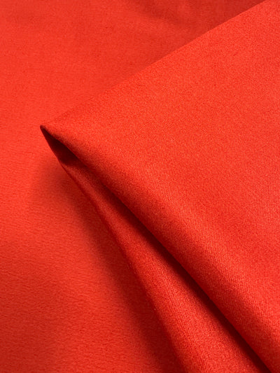 A close-up of Super Cheap Fabrics’ Plain Sateen - Aurora Red - 150cm, neatly folded at one corner, highlights its smooth texture and subtle sheen under soft lighting.