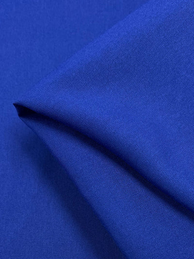 A close-up of a piece of smooth, neatly folded blue rayon fabric from the Super Cheap Fabrics' collection named "Plain Rayon - Turkish Sea - 140 cm," with a slightly visible diagonal texture. The lightweight material appears soft and evenly colored, reminiscent of the Turkish sea, with gentle shadows enhancing the folds and creases.