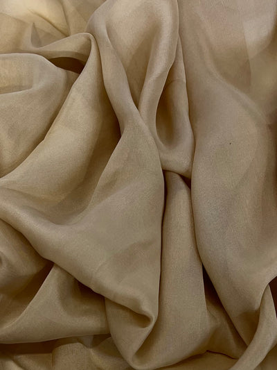 A close-up photograph of light beige, sheer fabric with soft folds and creases. The delicate, translucent Silk Chiffon - Pebble - 110cm from Super Cheap Fabrics has a smooth texture, creating a gentle play of light and shadow across its surface, perfect for dresses and skirts.