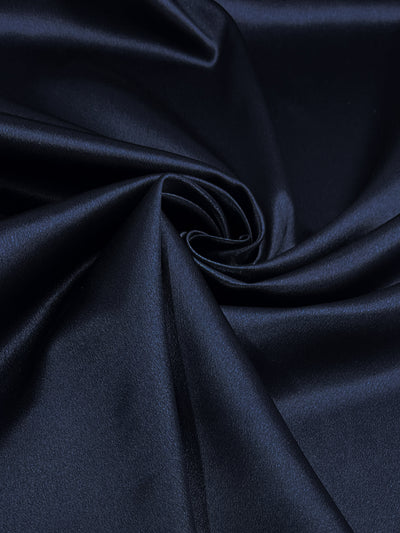 A close-up view of Super Cheap Fabrics' Satin Back Crepe - Navy - 150cm, gathered into a gentle swirl at the center. The fabric's sheen and texture are highlighted by subtle folds and light reflections, creating a sense of softness and elegance.
