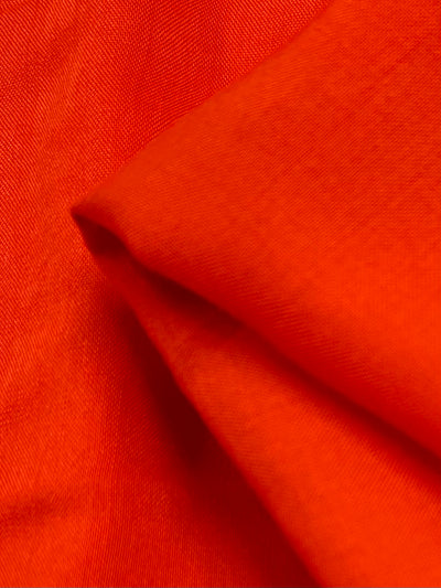 Close-up of vibrant, Plain Rayon - Mandarin - 140cm fabric from Super Cheap Fabrics with a smooth texture. This lightweight fabric is slightly folded, creating subtle shadows and variations in the hue. The overall appearance is vivid and captivating.