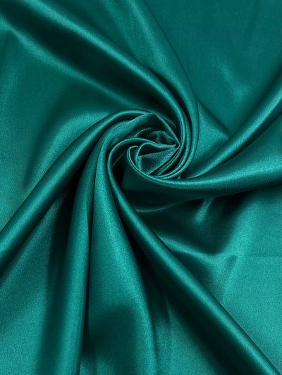 A close-up of Satin Deluxe - Slushy - 150cm satin fabric by Super Cheap Fabrics with a smooth, glossy surface. The material is gathered into a swirl pattern, creating folds and highlights that emphasize its luxurious texture, ideal for nightgowns and showcasing its vibrant color as a luxury fabric.