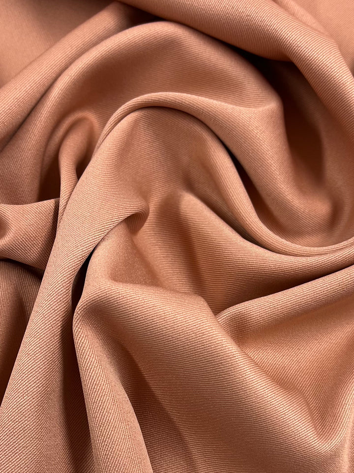 A close-up image of crumpled, soft, peach-colored Twill Suiting - Peach Bloom - 155cm by Super Cheap Fabrics with a smooth and slightly shiny texture. The folds and creases in the material create a wavy pattern, showcasing its fluid and delicate nature.