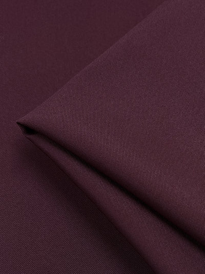 A close-up of a folded piece of Twill Suiting - Madder Brown - 155cm. The texture appears smooth and slightly ribbed, with visible thread lines running diagonally across the fabric, showcasing its diagonal weave pattern. The medium weight fabric is neatly folded, creating clean lines and subtle shadows. This quality product is brought to you by Super Cheap Fabrics.