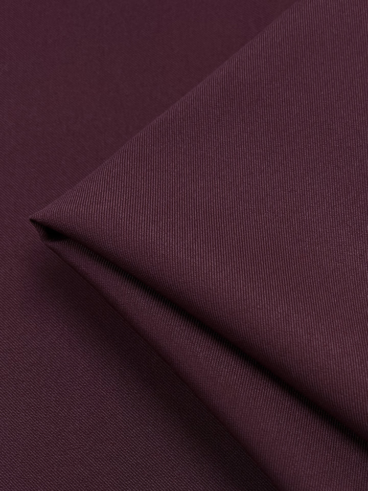 A close-up of a folded piece of Twill Suiting - Madder Brown - 155cm. The texture appears smooth and slightly ribbed, with visible thread lines running diagonally across the fabric, showcasing its diagonal weave pattern. The medium weight fabric is neatly folded, creating clean lines and subtle shadows. This quality product is brought to you by Super Cheap Fabrics.