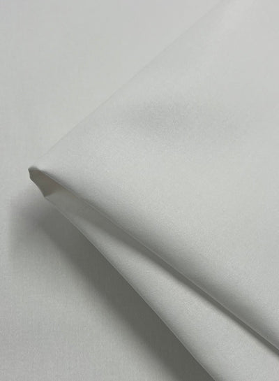 A close-up image of smooth, light gray Cotton Sateen - White - 150cm from Super Cheap Fabrics folded neatly, showcasing its soft texture and subtle sheen. The medium weight fabric appears to be lightweight and silky, with gentle folds and a clean, wrinkle-free surface.