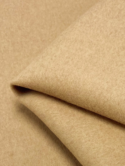 A close-up of the folded Wool Cashmere - Latte by Super Cheap Fabrics highlights its soft, smooth texture and cozy look. The extra heavy weight material's layered edge is prominently showcased in the center, illustrating elegant craftsmanship.