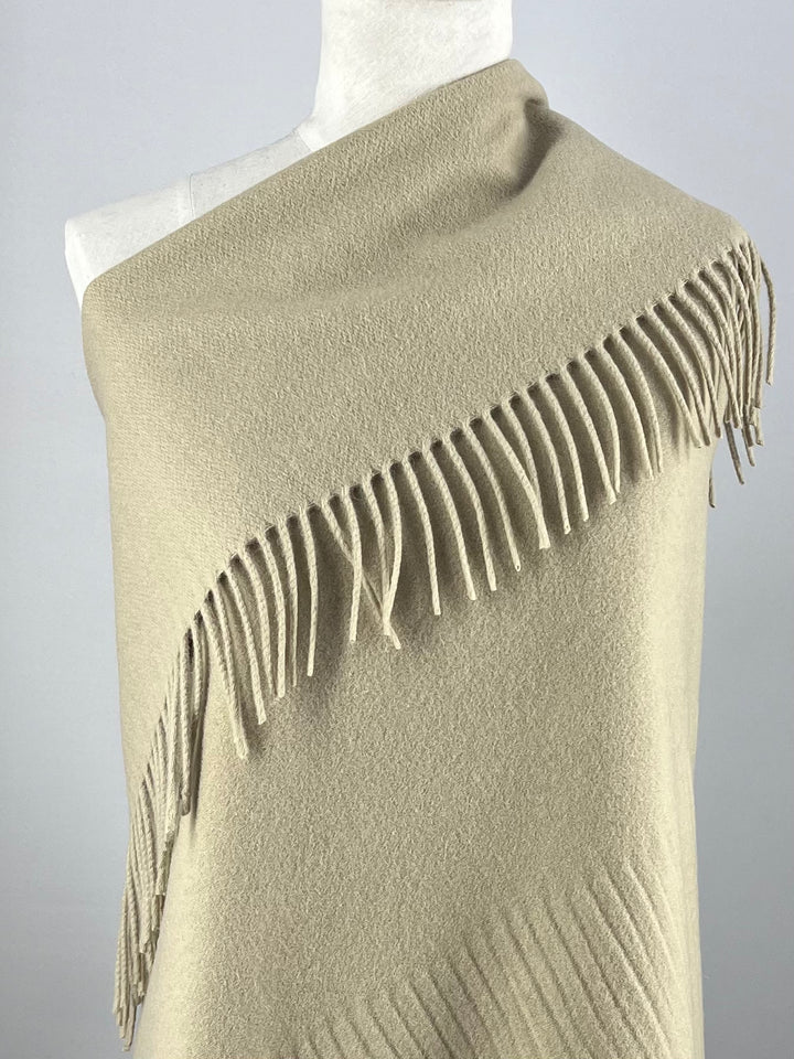 A mannequin showcases a pale olive green Merino wool shawl from Super Cheap Fabrics, draped over one shoulder. Its soft texture and elegant fringe create a refined look against a neutral background.