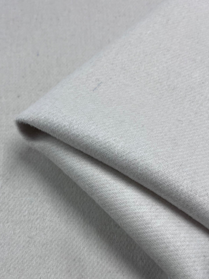 Close-up of folded Birch Wool Cashmere fabric by Super Cheap Fabrics, 150cm wide, in light gray. The material has a soft, textured surface with neatly aligned edges, appearing smooth and thick, implying high-quality for versatile use.