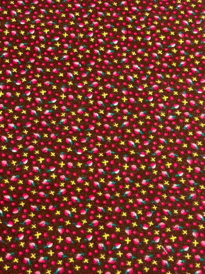 A light weight fabric with a dark brown background covered in a pattern of small, colorful floral elements. This versatile Printed Ramie Cotton - Colorful Flowers - 147cm from Super Cheap Fabrics includes tiny pink flowers, yellow stars, and small blue and green leaves evenly distributed across the surface, making it perfect for multiuse applications.