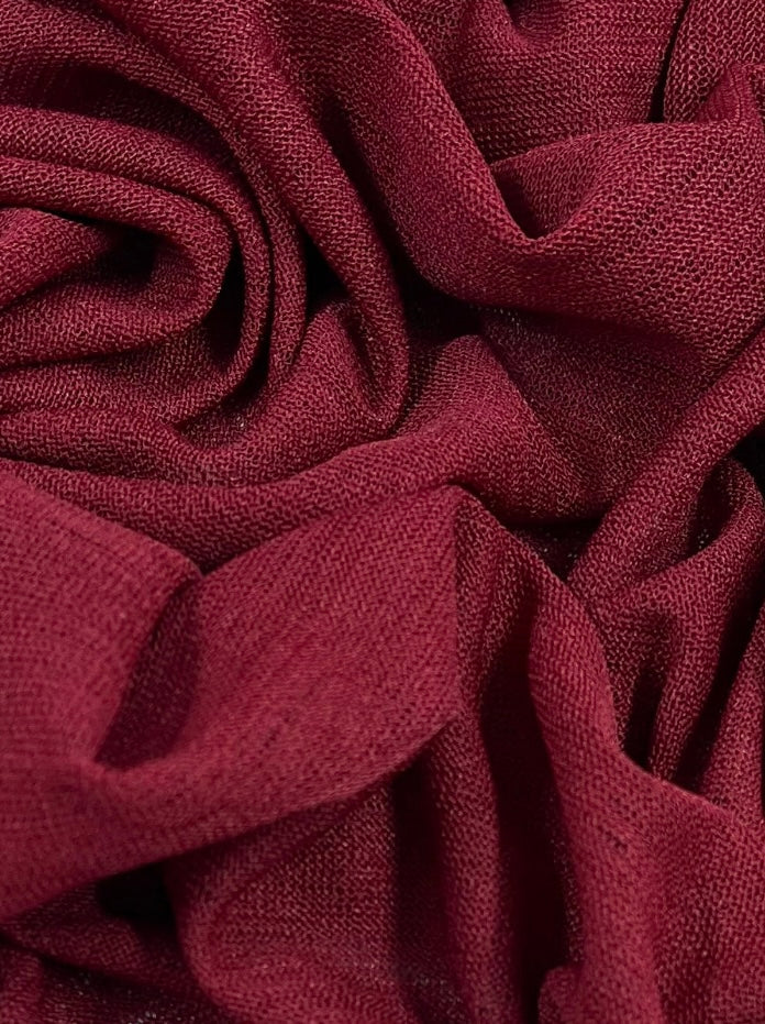 A close-up image of Super Cheap Fabrics Lightweight Slub Jersey - Scooter Red - 150cm with a coarse texture, artfully arranged in soft folds and overlapping layers. The textured knit material catches light and shadow, creating a rich, dynamic appearance.