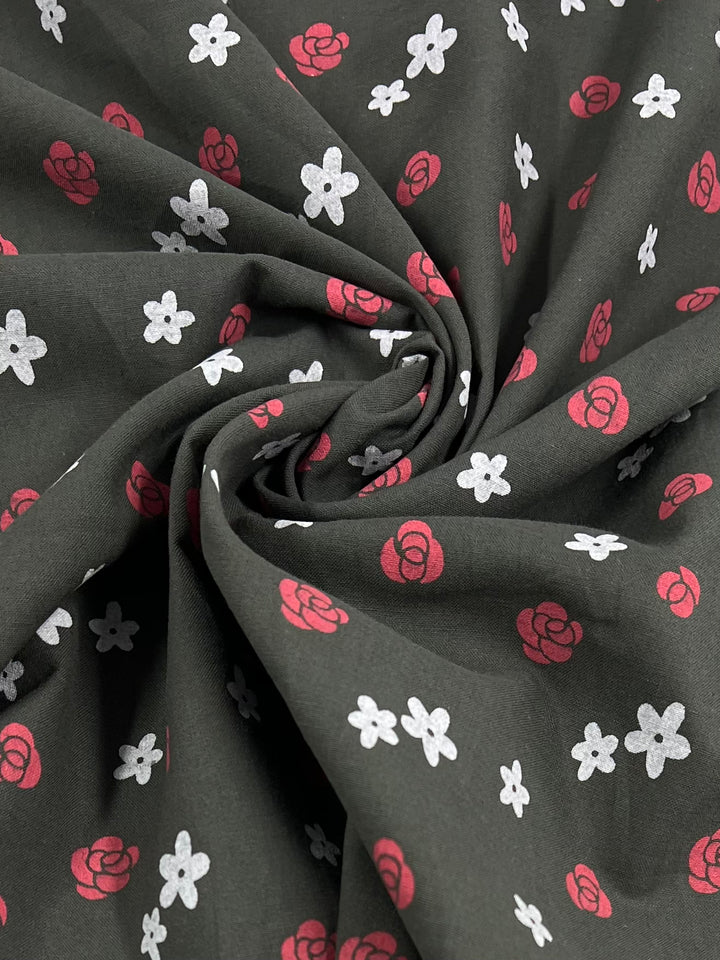 A close-up of the Linen Voile - Roses fabric, a dark green offering from Super Cheap Fabrics, showcases its elegant swirling pattern. Ideal for home decor, this 145cm wide material features red rose silhouettes and evenly distributed white flower shapes across its surface. The breathable fabric appears soft and slightly gathered at the center of the image.