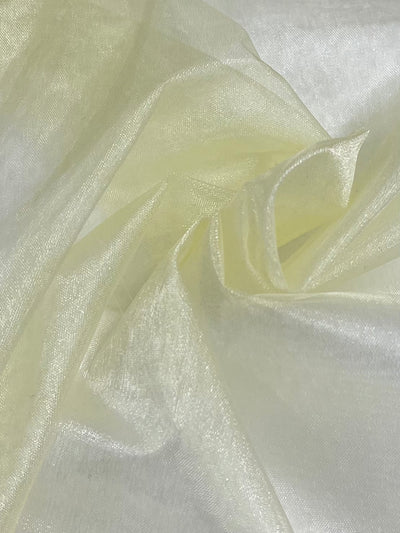 A close-up image of a piece of Organza - Pear Sorbet - 150cm fabric by Super Cheap Fabrics. The light yellow organza material is crumpled and folded, creating gentle waves and soft shadows. This lightweight fabric appears delicate and slightly glossy, reflecting light to give a subtle shimmer.