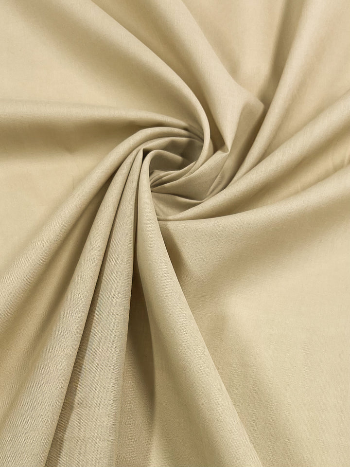 A close-up view of Super Cheap Fabrics' Cotton Voile - Putty - 140cm, folded and twisted into a spiral pattern, creating smooth, flowing lines and light shadow effects. The texture appears soft and smooth, with faint linear details visible throughout the material—ideal for elegant home decor.