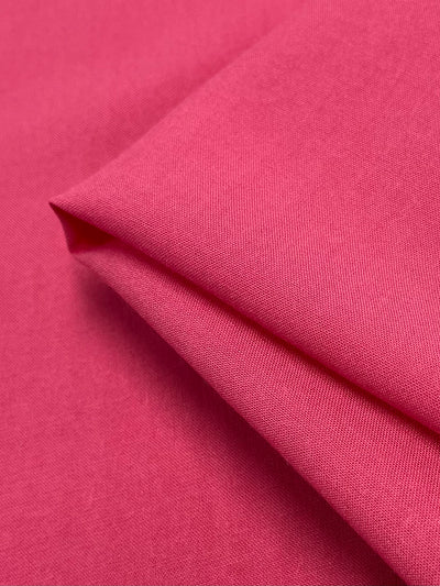 A close-up view of bright pink bubblegum fabric with a smooth, woven texture. The lightweight fabric, made from 100% rayon, is folded neatly, showcasing its soft and slightly reflective surface. This is the Plain Rayon - Bubblegum - 140cm by Super Cheap Fabrics.