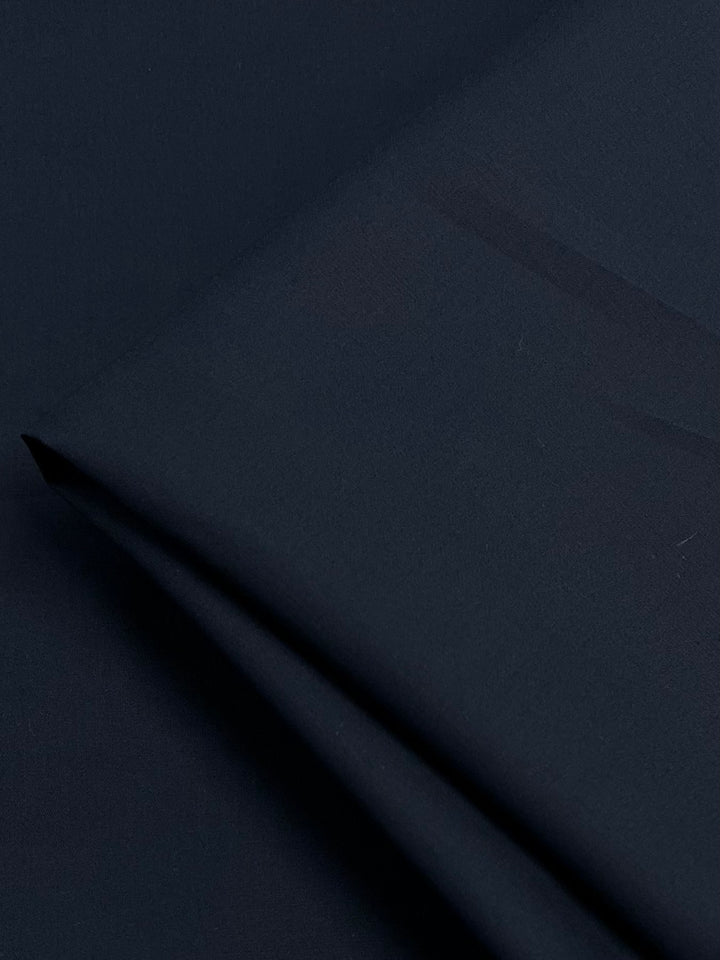 A close-up image of Super Cheap Fabrics' Mercerised Cotton - Navy - 150cm, neatly folded. The lightweight fabric appears smooth and slightly matte, with minor visible creases near the fold. The texture suggests a soft, possibly woven material.