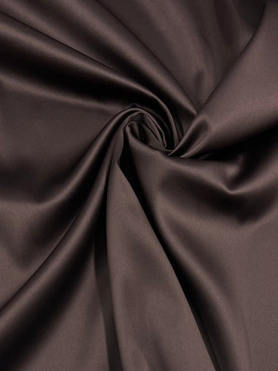 A close-up image of dark brown Satin Deluxe - Brown - 150cm fabric from Super Cheap Fabrics, arranged in a swirl, showcasing its glossy texture and soft folds for a truly luxurious finish.