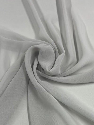 A close-up of Super Cheap Fabrics' Plain Georgette - Silver - 150cm that is sheer and flowing. The material is softly gathered into an elegant swirl, demonstrating its lightweight and translucent texture. The smooth folds create a gentle, airy appearance.