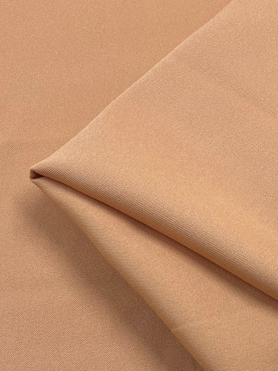 Close-up of a folded piece of **Super Cheap Fabrics Twill Suiting - Copper Tan - 155cm** displaying a smooth, textured surface with a subtle diagonal weave pattern. The fabric appears to be soft and slightly reflective, suggesting a fine, high-quality material suitable for garments or upholstery.