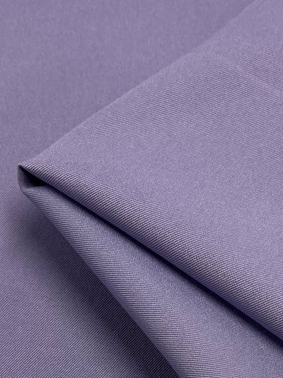 A close-up of a neatly folded piece of Twill Suiting - Sweet Lavender - 155cm from Super Cheap Fabrics with a smooth, slightly glossy texture. The tightly woven diagonal weave fabric displays fine details, showcasing its quality and finish perfect for versatile garments.