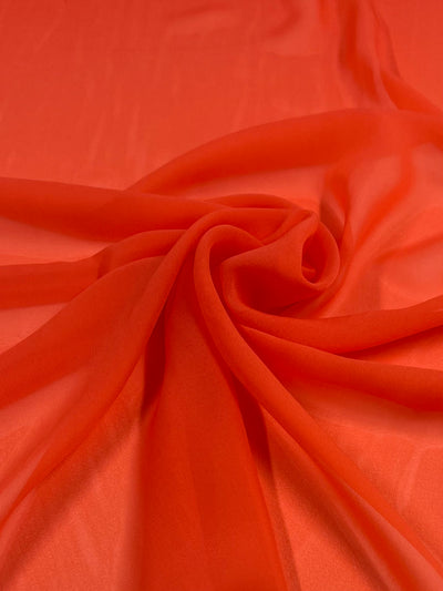 A smooth piece of Super Cheap Fabrics' Hi-Multi Chiffon - Coral Quartz - 150cm is draped and slightly gathered in a spiral at the center of the image. The lightweight material appears sheer, with soft folds and gentle shadows.