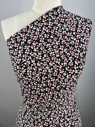 A black dress made from Super Cheap Fabrics' Printed Lycra - Moonwalk - 150cm, with a one-shoulder design and a pattern of small pink and white flowers, is displayed on a mannequin against a plain gray background.
