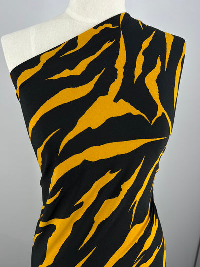 A close-up of a mannequin dressed in a one-shoulder garment featuring a bold black and yellow tiger stripe pattern. The medium weight fabric, likely Printed Lycra - Claw - 150cm by Super Cheap Fabrics, has a smooth texture, creating a striking visual contrast. The background is plain and light-colored.