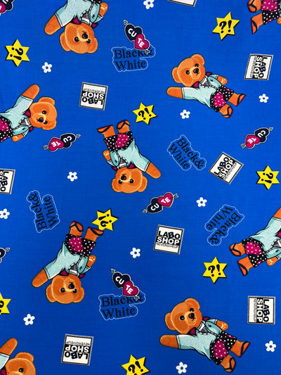 A blue fabric features a pattern with orange teddy bears in various poses wearing blue outfits. The design includes scattered text reading "Black & White" and "LABO SHOP" along with images of stars, keys, and question marks. Ideal for dresses, this Printed Rayon - Royal Bear - 145cm by Super Cheap Fabrics is both playful and stylish.