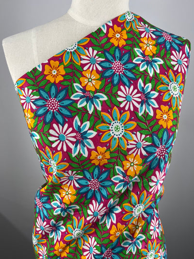 A close-up of a white mannequin draped in lightweight, floral-patterned fabric. The Printed Rayon - Lolita Spring - 145cm from Super Cheap Fabrics, adorned with large, vibrant flowers in shades of blue, yellow, white, pink, and green on a purple background, stands out against the plain gray backdrop.
