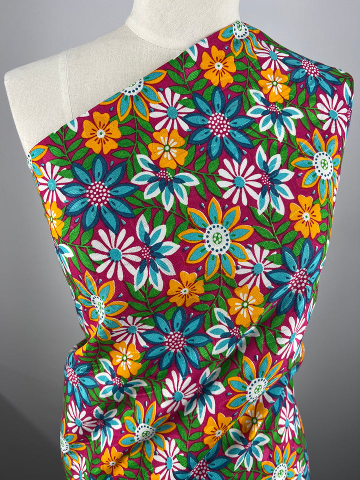 A close-up of a white mannequin draped in lightweight, floral-patterned fabric. The Printed Rayon - Lolita Spring - 145cm from Super Cheap Fabrics, adorned with large, vibrant flowers in shades of blue, yellow, white, pink, and green on a purple background, stands out against the plain gray backdrop.