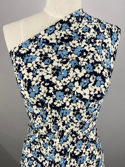 A close-up view of a dress mannequin wearing a one-shoulder dress made from medium-weight fabric. The dress showcases a black, white, and blue floral pattern using Printed Lycra - Blu Density - 150cm by Super Cheap Fabrics. The background is plain and gray.