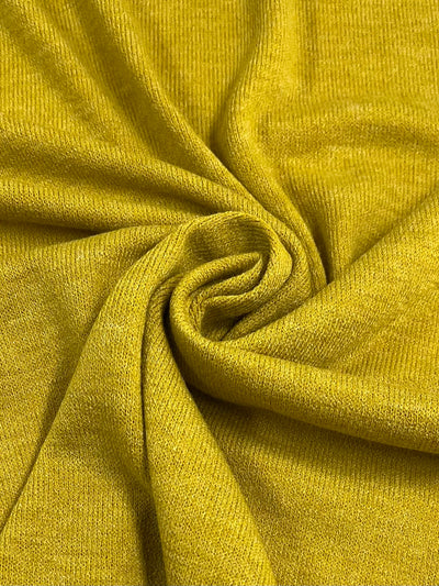 A close-up view of Textured Knit - Gold Flake - 145cm by Super Cheap Fabrics with a soft texture. The fabric is gathered in the center, forming gentle folds and curves, creating a spiral-like design. The material appears smooth and slightly stretchy, perfect for elegant dresses.