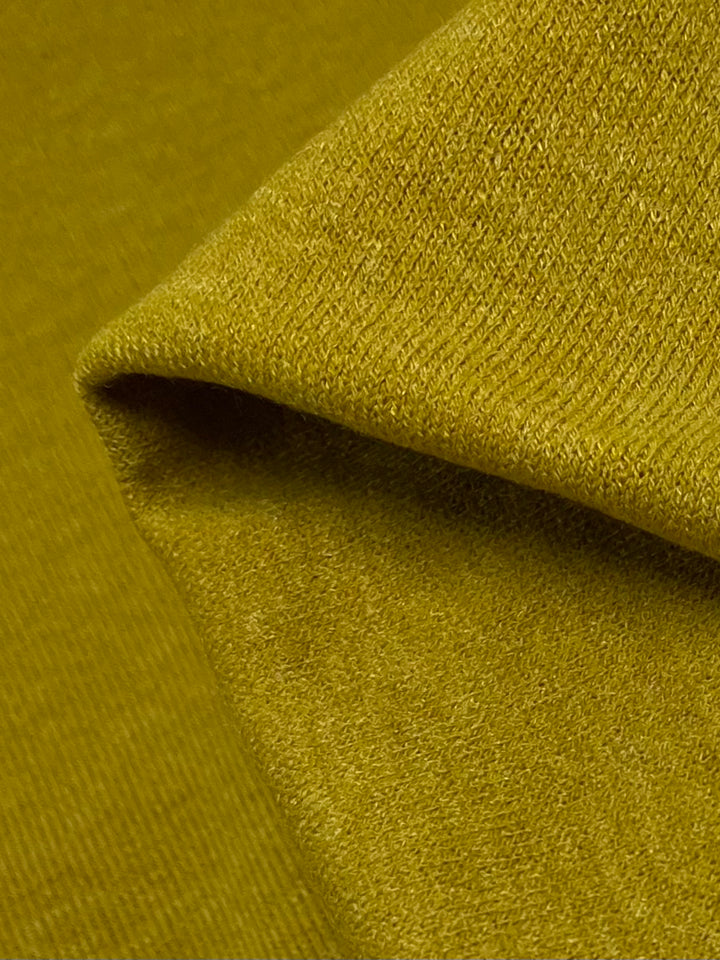 Close-up image of a folded piece of Super Cheap Fabrics Textured Knit - Gold Flake - 145cm, showing its textured surface. The medium weight fabric appears soft and has a visible weave pattern, with one edge neatly tucked and overlapping another part of the material.